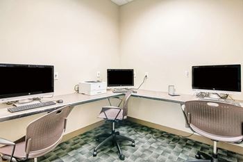 A room with a desk, chairs and computer monitors.